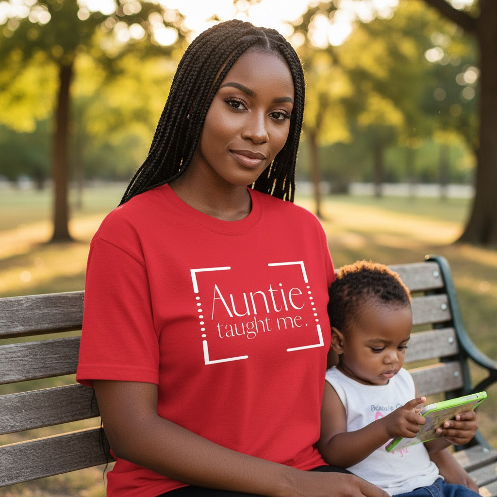 Woman in a red 'Auntie taught me' shirt sitting on a bench with a child.