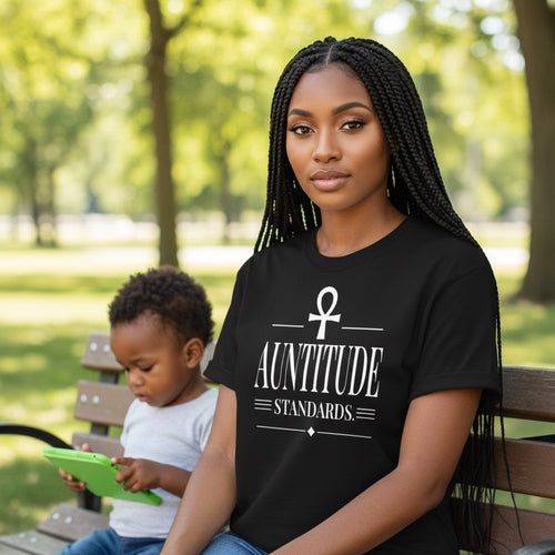 Woman wearing a black t-shirt with 'Auntitude Standards' design sitting on a park bench with a child.