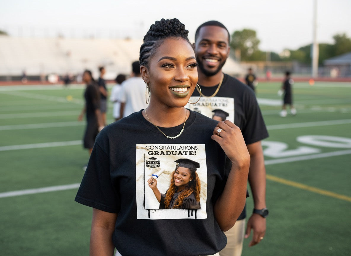Woman wearing a graduation-themed t-shirt with a man standing behind her on a sports field.