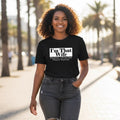 Woman wearing a black t-shirt with text, standing outdoors with palm trees in the background
