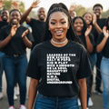 Woman wearing a black t-shirt with text, standing in front of a group of people.