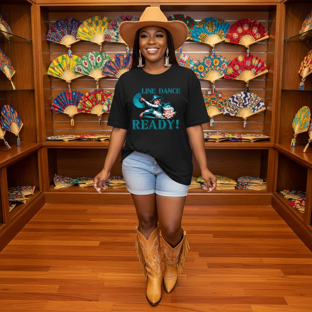 Woman in a black t-shirt with a colorful design, light blue shorts, and tan cowboy boots standing in front of a display of decorative fans.