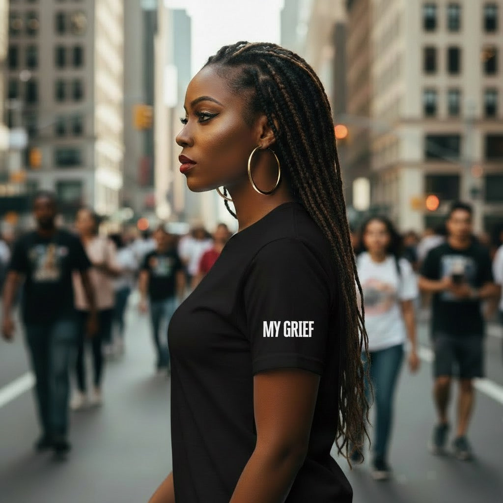 Woman wearing a black t-shirt with 'MY GRIEF' text on a city street.