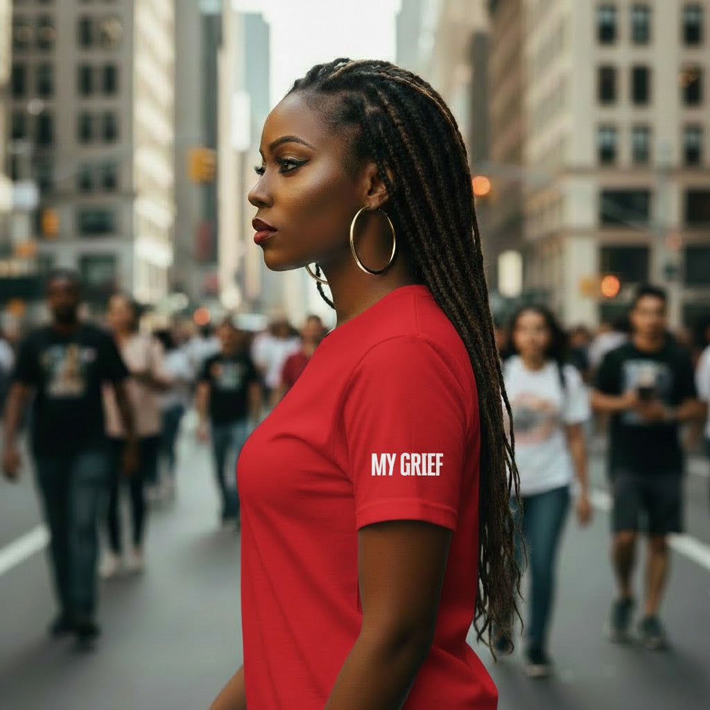 Woman wearing a red shirt with 'MY GRIEF' text on a city street.