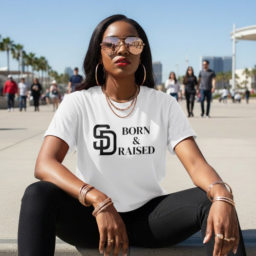 Woman wearing a 'Born & Raised' t-shirt sitting outdoors with a cityscape background