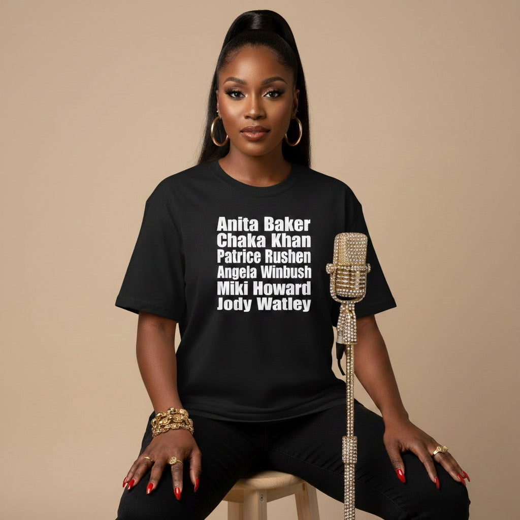 Woman wearing a black t-shirt with names on it, sitting on a stool against a beige background