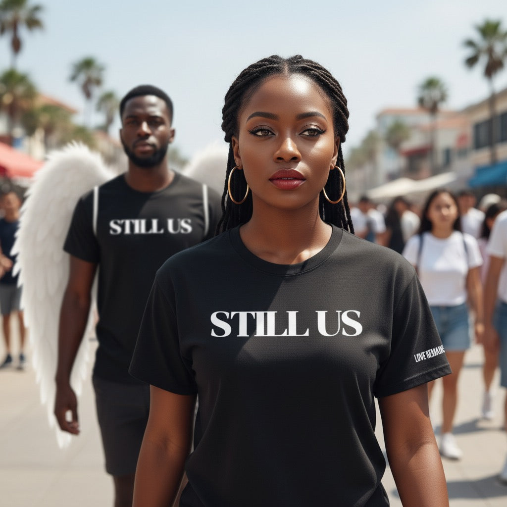 Woman wearing a 'STILL US' t-shirt with a blurred background of people and palm trees.