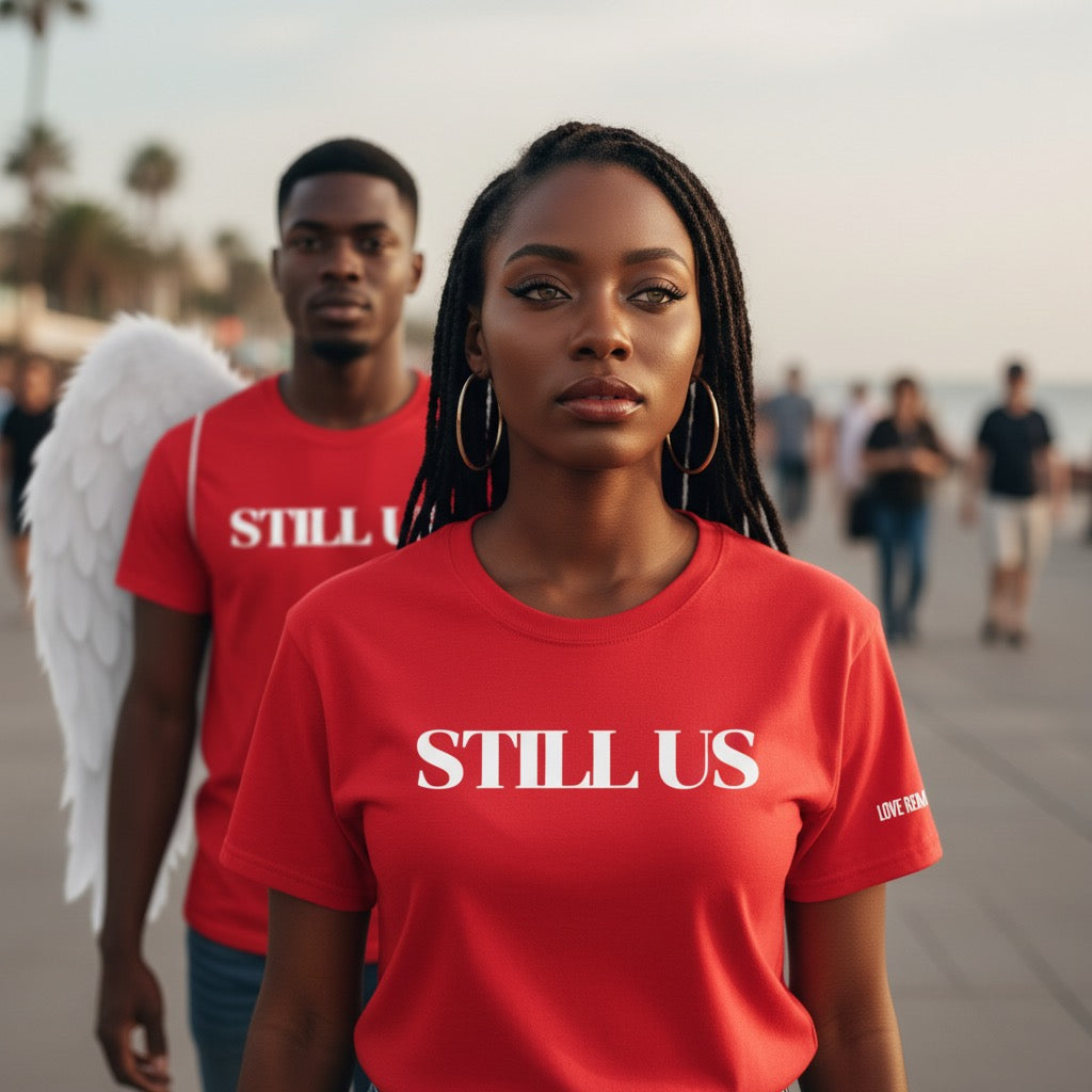 Two people wearing red 'STILL US' t-shirts on a beach.
