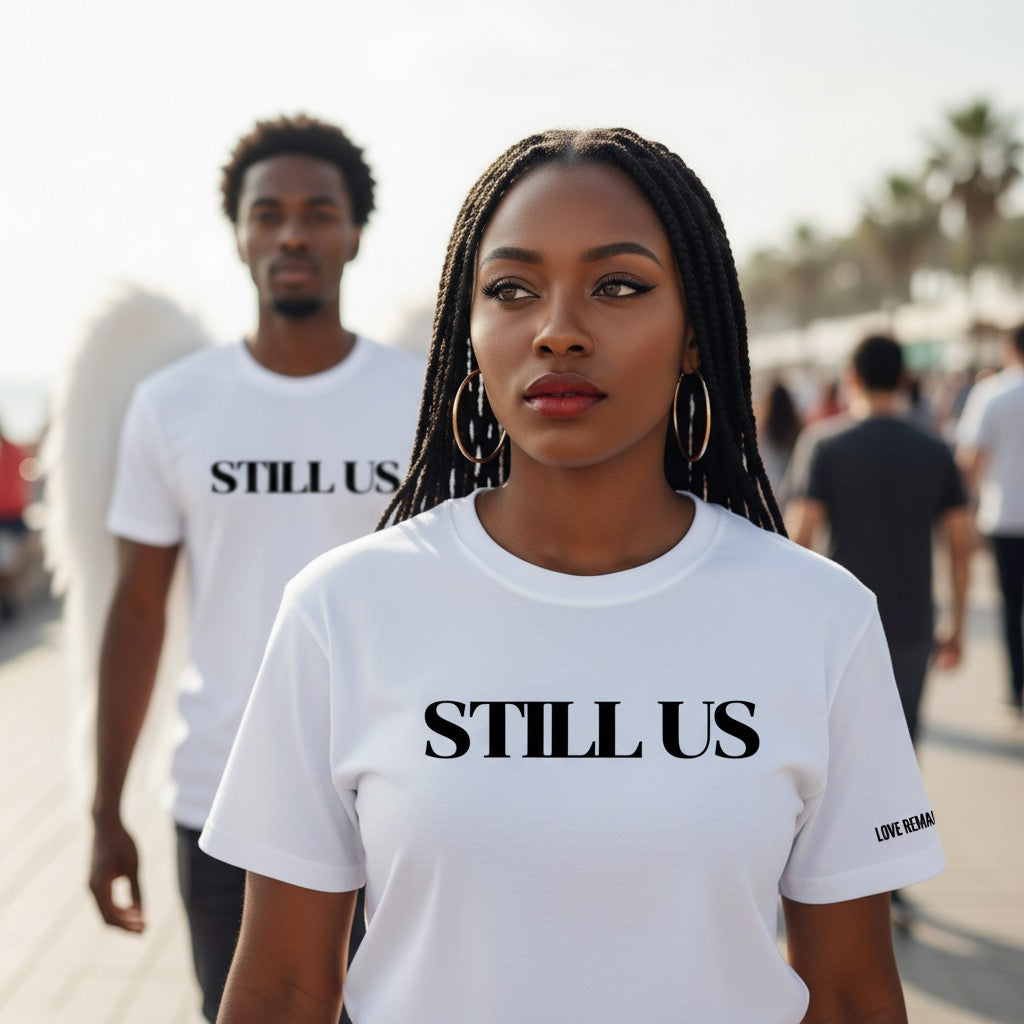 Two people wearing 'STILL US' t-shirts in a casual outdoor setting.