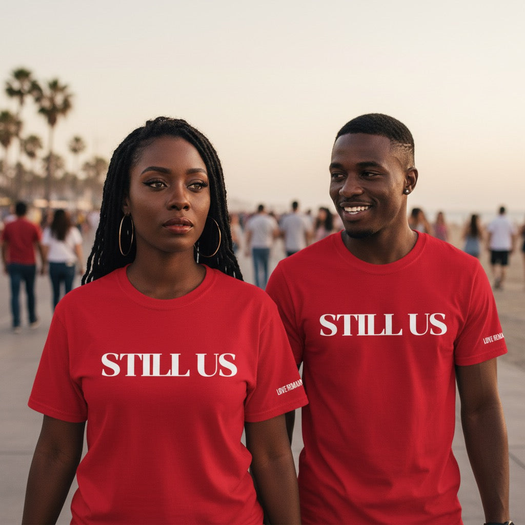 Two people wearing 'STILL US' shirts on a beach.