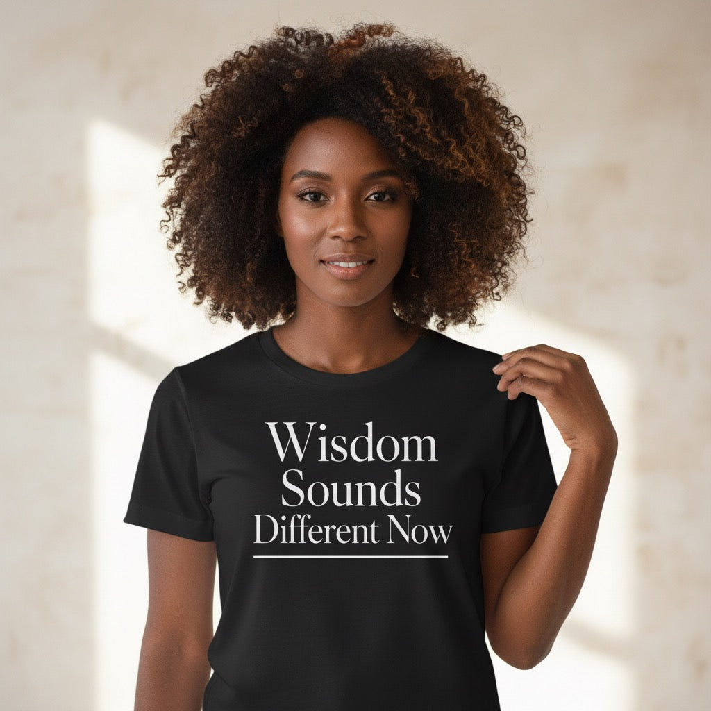 Woman wearing a black t-shirt with 'Wisdom Sounds Different Now' text against a neutral background