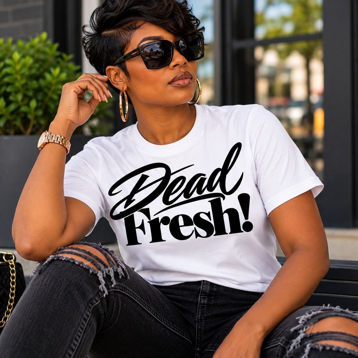 Woman wearing the white Dead Fresh! graphic T-shirt with black lettering and styling it with black jeans and gold accessories.