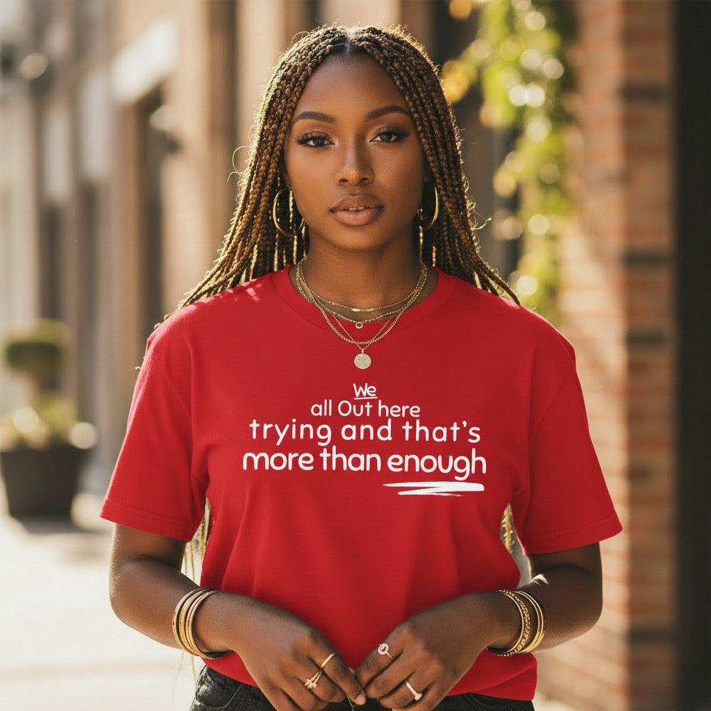 Black woman wearing the The Trying Is in the Triumph statement t-shirt featuring the phrase "We all out here trying and that's more than enough."