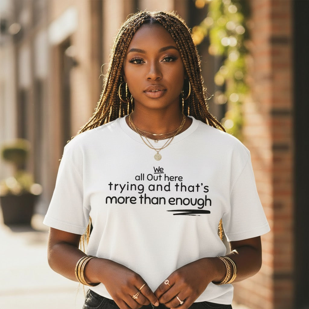 Black woman wearing the The Trying Is in the Triumph statement t-shirt featuring the phrase "We all out here trying and that's more than enough."